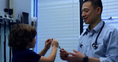 Genç Asyalı erkek doktor gösteren tuning çatal beyaz çocuk hastada klinik için yan görünüm. Erkek doktor hasta 4 k ile etkileşim