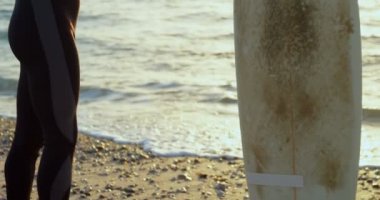 Yan görünüm Plajı'nda sörf önce ısınma ve germe yetişkin beyaz erkek sörfçü. 4k arka planda güzel gün batımı