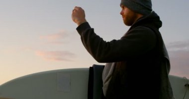 Yan görünümü yetişkin beyaz adamın cep telefonu Sahil yakınındaki ile fotoğrafı tıklatın. Adam 4 k surfboard ile ayakta