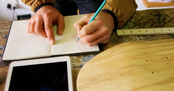 在车间里用铅笔写日记的年轻人的特写镜头 表4K 上的数字平板电脑和滑板 — 图库视频影像