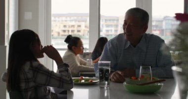 Sevimli Asya torunu ve konforlu bir evde yemek yeme eski üst düzey büyükbaba. Büyükanne ve torunu 4 k arka planda masada oturan