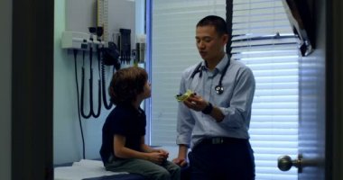 Genç Asyalı erkek doktor gösteren kulak model beyaz çocuk hastada klinik için yan görünümü. Erkek doktor hasta 4 k ile etkileşim