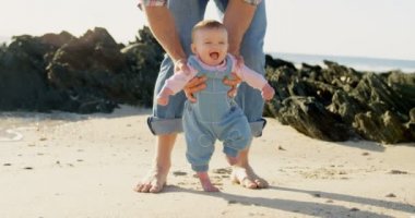 Önden görünüm bir orta yetişkin beyaz baba bebek plajda güneşli bir günde yürümek için yardım. Bebek 4 k yürümeyi öğrenmek