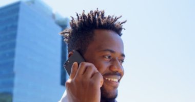 Hareket eden telefon içinde balkon modern ofis konuşurken genç siyah işadamı düşük açılı görünümü. Güneşli bir günde 4 k balkonda duran işadamı