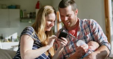 Önden görünüm fotoğrafları cep telefonu rahat bir ev içinde gözden yetişkin beyaz ebeveynler orta. Baba süt onun bebek besleme şişe 4 k