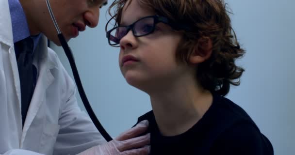 アジアの若い男性の側面図は医師試験クリニックで白人少年患者胸部です の聴診器を使用して男性医師 — ストック動画