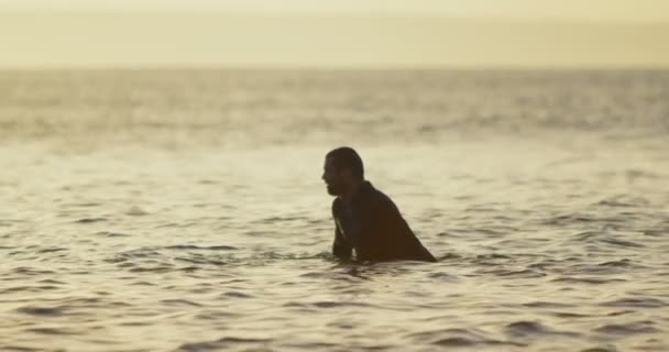日没時に海でサーフボードの上に座って半ば成人白人男性サーファーの側面図です を探している男性のサーファー — ストック動画