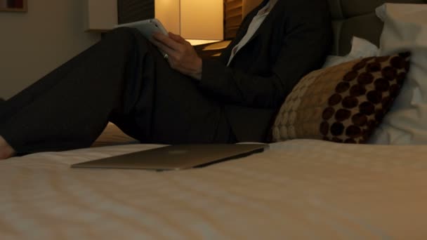 モダンなホテルは デジタル タブレットに取り組んで半ば大人白人実業家の側面図です のベッドに座ってラップトップを持つ実業家 — ストック動画