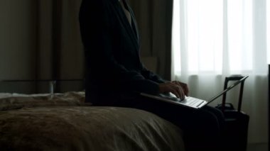 Yetişkin beyaz işkadını üstünde laptop modern bir otelde çalışan yan görünüm. 4 k yatağa oturmuş işkadını