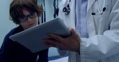Genç Asyalı erkek doktor ve beyaz çocuk hastanın klinik dijital tablet kullanarak önden görünümü. Erkek doktor hasta 4 k ile etkileşim