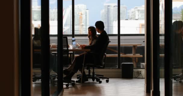 近代的なオフィスに互いと対話する若いアジア ビジネス同僚の側面図です のテーブルに座って若いアジア ビジネス部門の同僚 — ストック動画