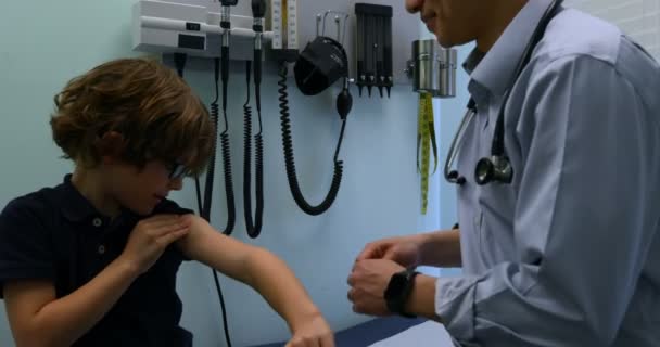 アジアの若い男性のサイドビューは医師クリニックで白人少年患者の腕に適用するバンド エイドです 男性医師患者 との相互作用 — ストック動画