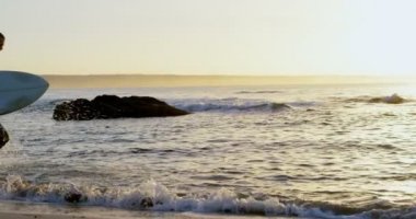 Yetişkin beyaz erkek sörfçü günbatımı sırasında denizde çalışan surfboard ile yan görünüm. 4k planda sakin deniz