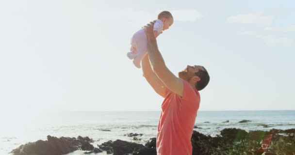 晴れた日にビーチで空気中半ばの大人の白人父持株赤ちゃんの側面図です 赤ちゃん で遊んでの父 — ストック動画