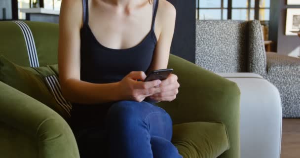 近代的なオフィスに携帯電話で話していると若い白人実業家テキスト メッセージのフロント ビュー のソファに座って実業家 — ストック動画