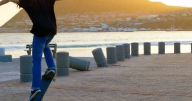 Arka bakış beyaz delikanlı beach promenade günbatımı sırasında kaykay ile atlama. Kaykay hüner 4 k yapan erkek