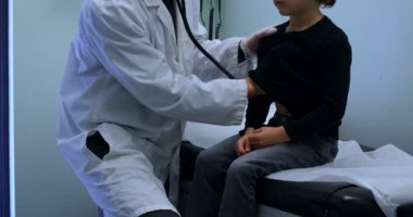 Genç Asyalı erkek yan görünüm doktor bir klinik muayene beyaz çocuk hastanın göğsünden. Erkek doktor stetoskop 4 k kullanma