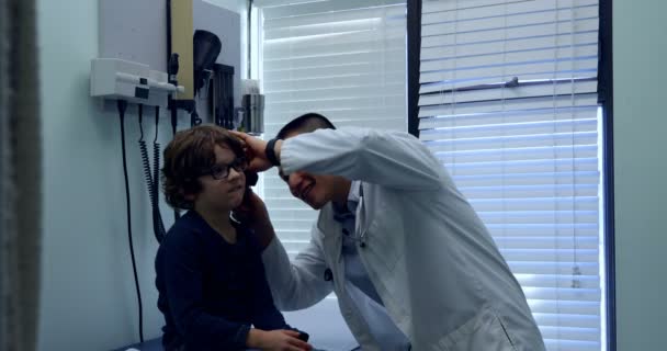 Вид Сбоку Молодого Врача Азиата Осматривающего Больное Ухо Кавказского Мальчика — стоковое видео