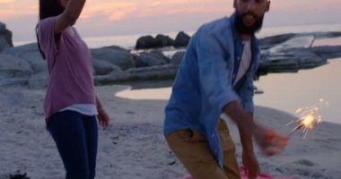 Havai fişekleri ile eğleniyor kumsalda mutlu karışık ırk genç bir çift. karışık yarış çift sahilde günbatımı 4k sırasında