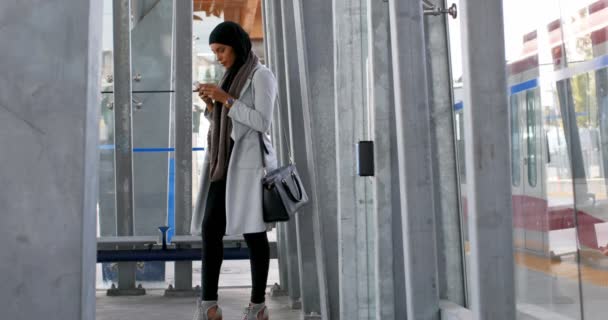 ヒジャーブ列車 を待っている鉄道駅若いアジア女性で携帯電話を使用しての若いアジア女性の側のビュー — ストック動画