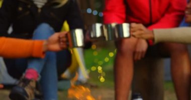 Kahve bardağı yakınındaki ormanda kamp ateşi toasting arkadaşlar. Birlikte 4 k ormanda kamp arkadaşları