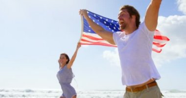 Beach adlı Amerikan bayrağı sallayarak tutan genç çift yan görünüm. Onlar 4 k kumsalda eğleniyor musun