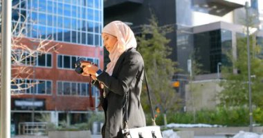Şehrin dijital kamera ile fotoğraf tıklayarak hijab genç Asyalı kadın yan görünüm. Şehir hayatı içinde belgili tanımlık geçmiş 4k