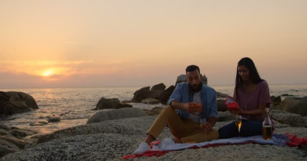 愉快的混血儿夫妇在海滩日落时互相赠送礼物 在海滩4K 的岩石上坐在岩石上的混血儿 — 图库视频影像
