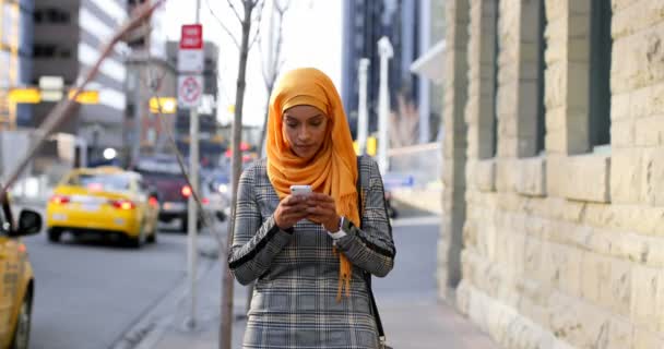 亚洲年轻女子在城市中使用手机戴头巾的正面观点 她站在人行道上看着4K — 图库视频影像
