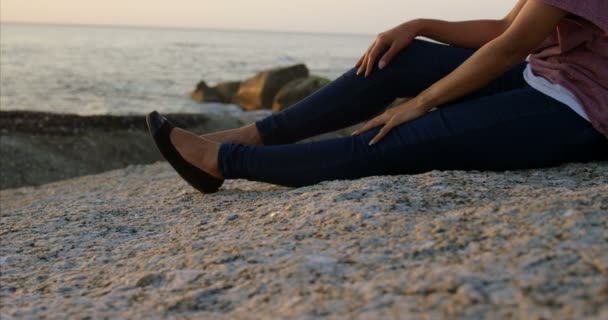 日落时 坐在沙滩上的岩石上的体贴的混血女人 在海4K 的混合种族妇女 — 图库视频影像