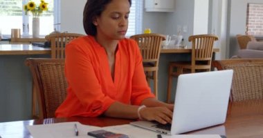 Karışık yarış Olgun kadın evde masa laptop çalışma önden görünümü. O bir belge 4 k yazıyor