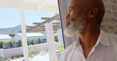 Düşünceli olgun siyah adam rahat bir ev penceresinde yakınındaki ayakta yan görünüm. 4 k pencereden bakıyor