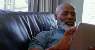 Olgun zenci dijital tablet içinde rahat bir ev kullanarak önden görünümü. O gülümseyen ve 4 k kanepede rahatlatıcı