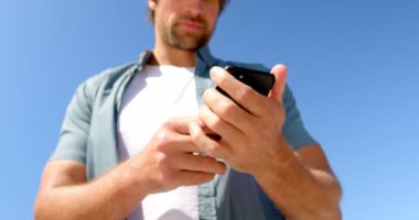 Güneşli bir günde beach adlı cep telefonu kullanan adam düşük açılı görünümü. 4k arka planda açık gökyüzü