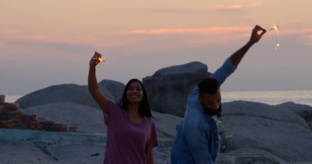 快乐的年轻混血夫妇有乐趣与火花在海滩上 日落时在海滩的混血儿4K — 图库视频影像