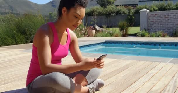 在家里的后院使用智能手机的年轻混血女子的侧视图 她在发短信 坐在阳光下4K — 图库视频影像