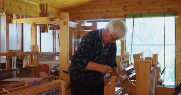 ワーク ショップで手織り機マシン上で動く古い白人の年配の女性のフロント ビュー 彼女はビーム でスレッドを結びです — ストック動画