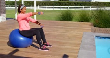 Karışık yarış Olgun kadın güneşli bir günde arka bahçe dumbbells ile egzersiz. O güneş 4 k dumbbells kullanıyor