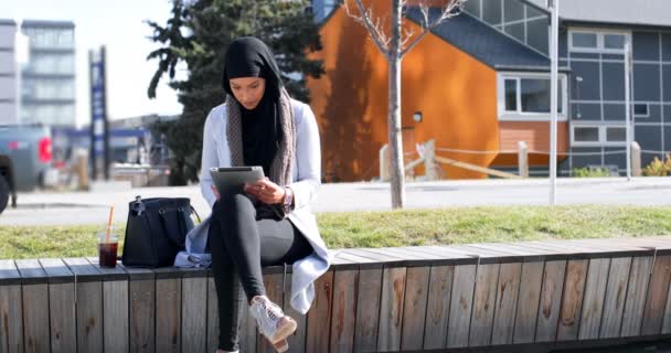 亚洲年轻女子在城市中使用数字平板电脑戴头巾的正面观点 年轻的亚洲妇女喝冷饮4K — 图库视频影像