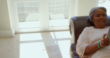 Evde oturma odasında dijital tablet kullanarak karma yarış kadın kıdemli. O 4 k evde kanepede rahatlatıcı