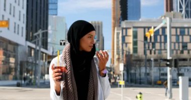 Şehir içinde cep telefonu konuşurken hijab genç Asyalı kadın önden görünümü. Soğuk içecek 4 k tutan genç Asyalı kadın