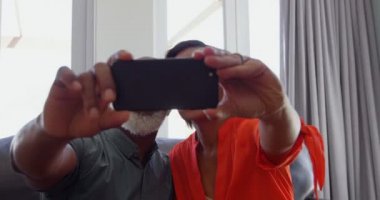 Olgun siyah çift tıklayarak selfie rahat bir ev içinde hareket eden telefon ile önden görünümü. Gülümseyen ve 4 k poz