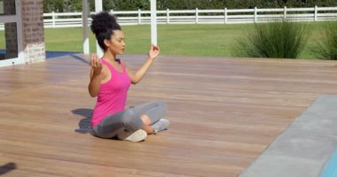 Karışık ırk kadın evinin arka bahçesinde yoga yaparken yan görünüm. 4 k gün ışığında Kapalı gözlerle meditasyon yapıyor