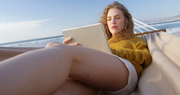 女性はビーチでハンモックでデジタル タブレットを使用します のハンモックでリラックスできる女性 — ストック動画