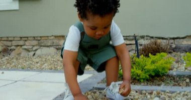 Şirin küçük siyah bebek evlerinin arka bahçesinde oynarken önden görünümü. Çakıl taşları 4 k atıyor