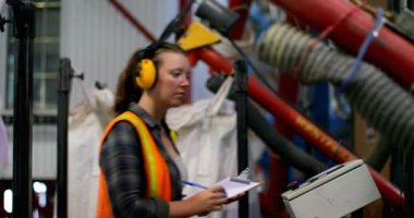 Genç bir beyaz kadın işçi fabrika stoklarında kontrol yan görünüm. Genç bir beyaz kadın işçi üstünde not etmek 4 k yazma