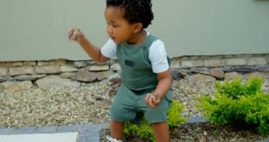 Şirin küçük siyah bebek evlerinin arka bahçesinde oynarken önden görünümü. Çakıl taşları 4 k atıyor