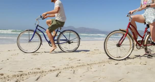 カップルの晴れの日にビーチで自転車に乗って 穏やかな海と美しい空背景 — ストック動画