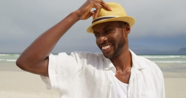在阳光明媚的日子里 男人站在沙滩上戴帽子 背景中的海浪4K — 图库视频影像