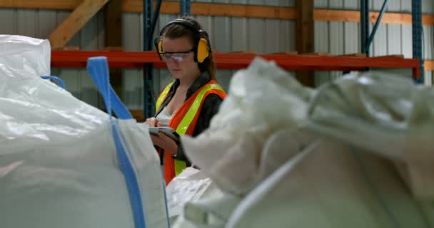 倉庫でデジタル タブレットに取り組んでいる白人の女性労働者のフロント ビュー フォア グラウンド にパックされた商品と高いラック — ストック動画